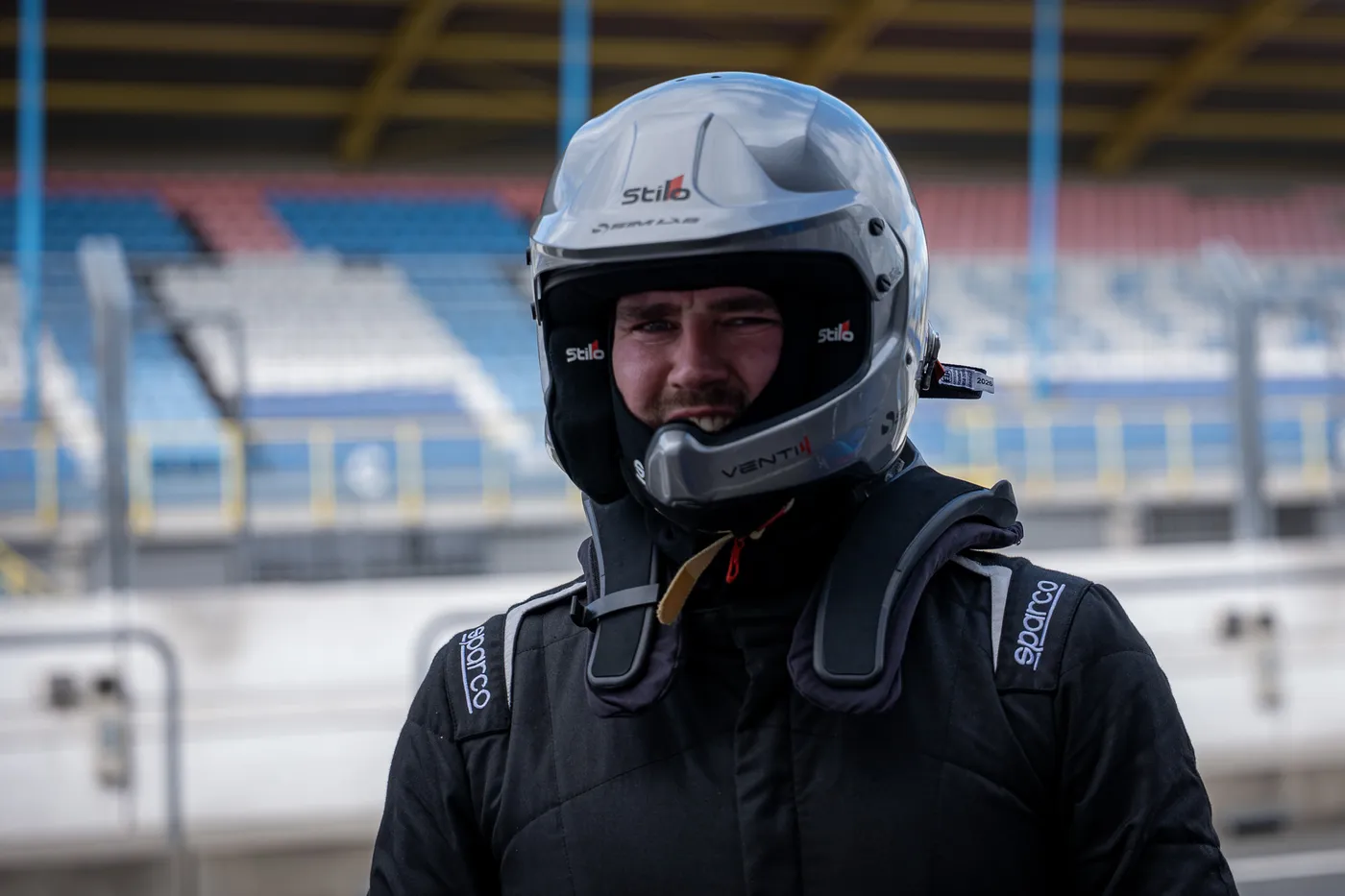 A driver in a white helmet smiling in the pit lane at Assen